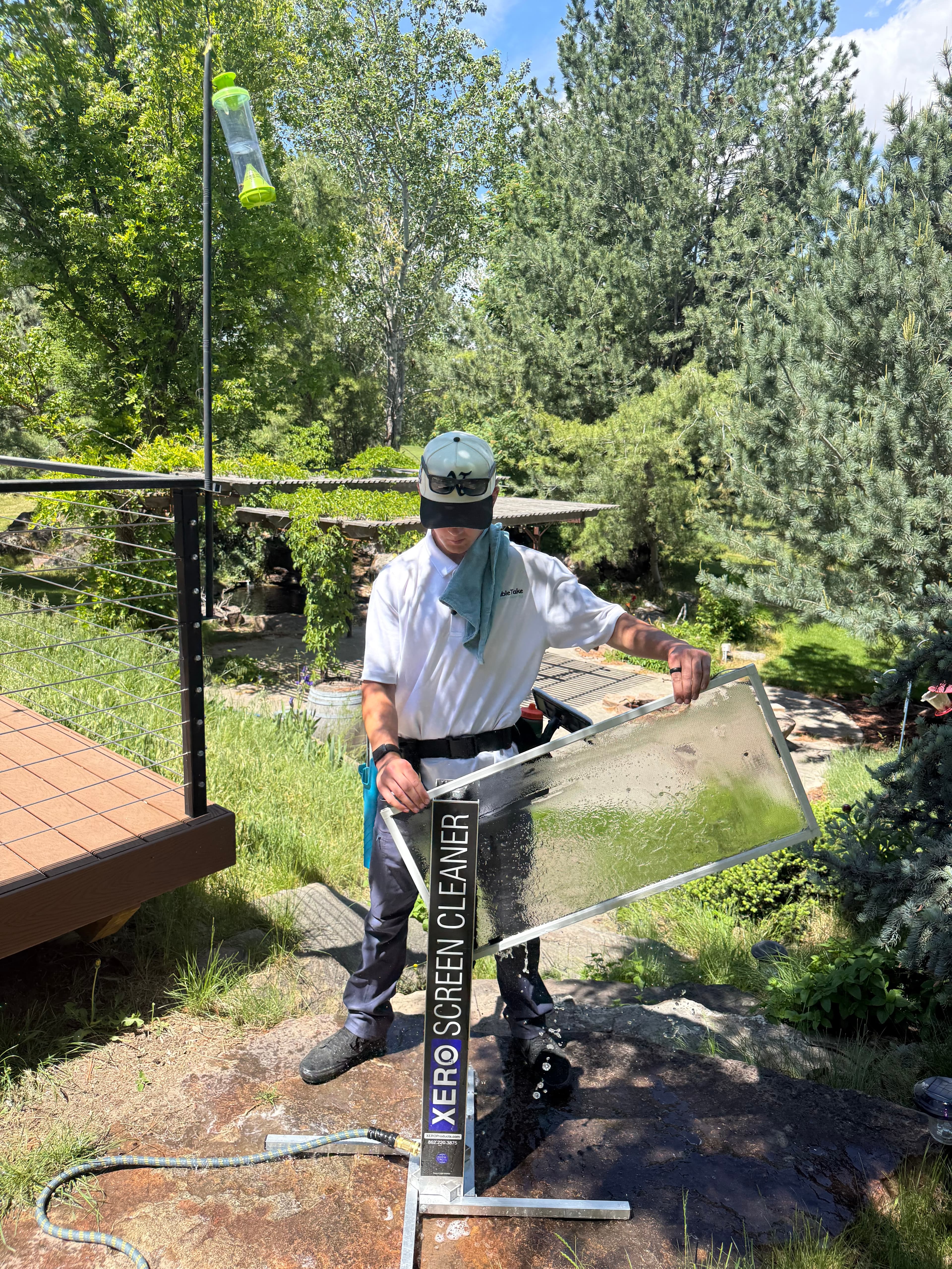 Professional cleaner uses a Xero Screen Cleaner machine to wash a window screen outdoors.