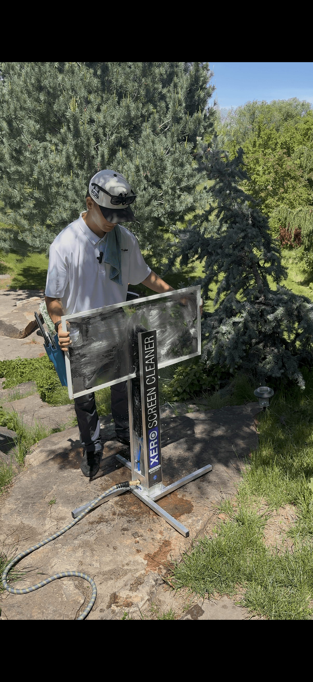 Man cleaning a window screen using a XERO Screen Cleaner machine on a sunny stone patio.