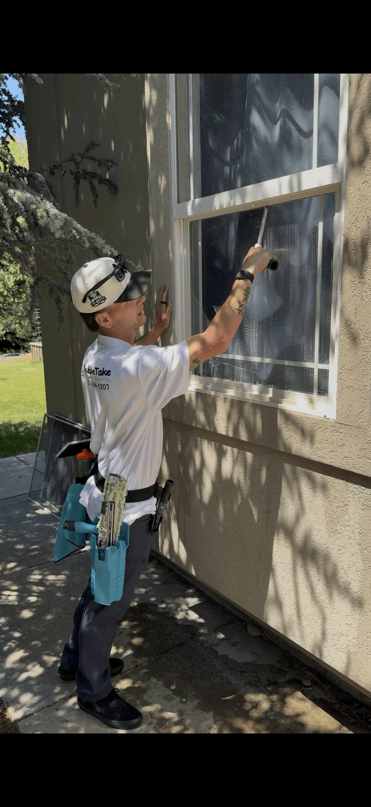Professional window cleaner in a white shirt uses a squeegee on an exterior house window.