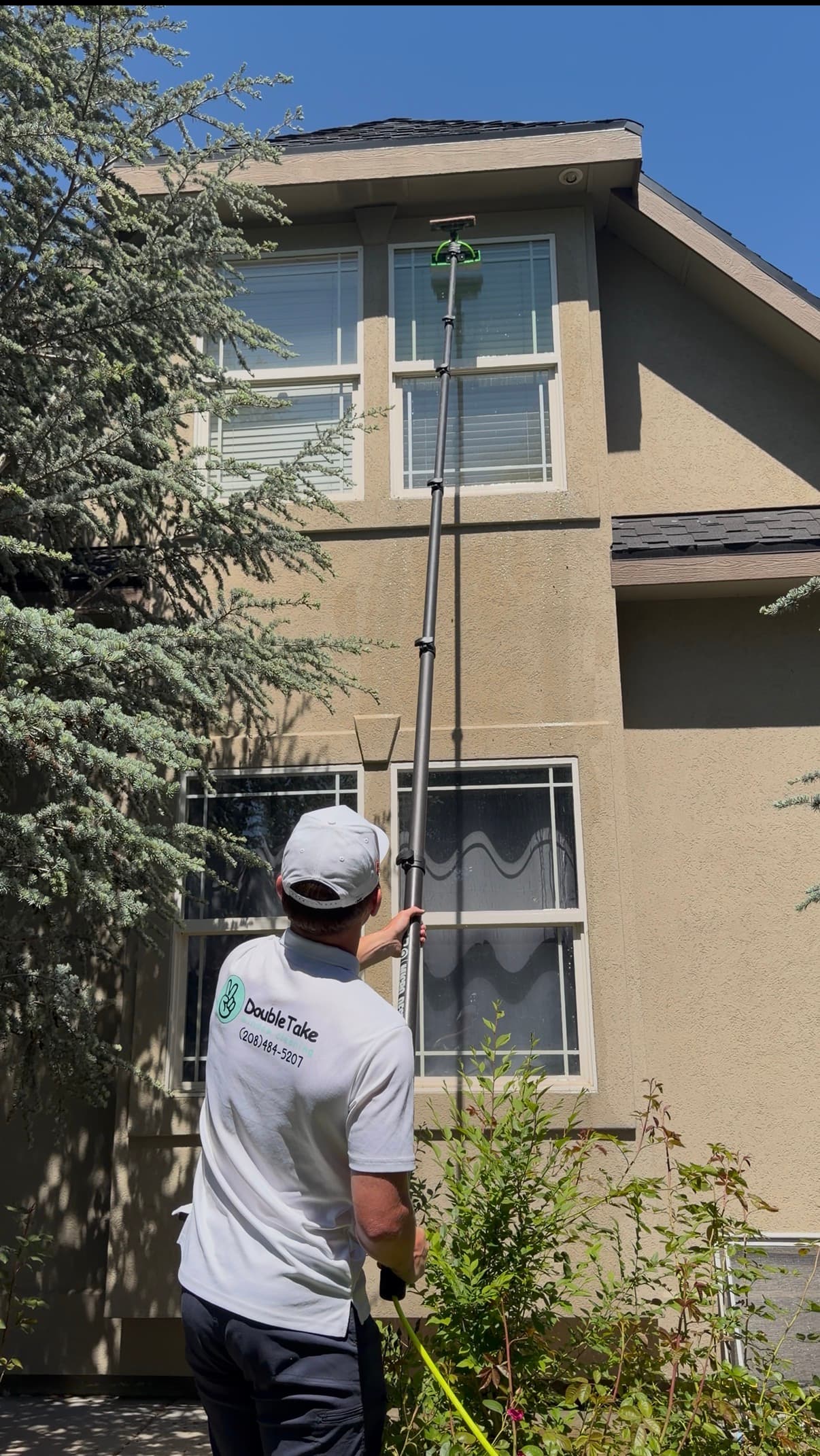 Professional window cleaner uses a long telescopic pole to wash high windows of a house.