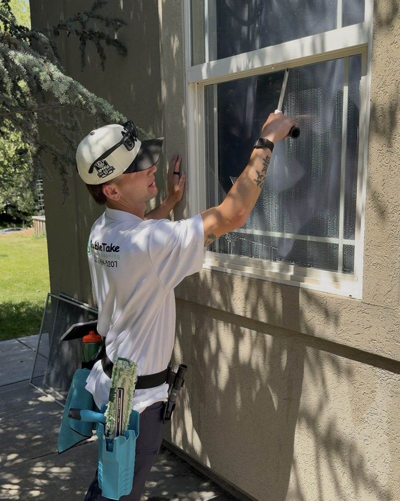 Professional window cleaner in a white shirt uses a squeegee on an exterior house window.