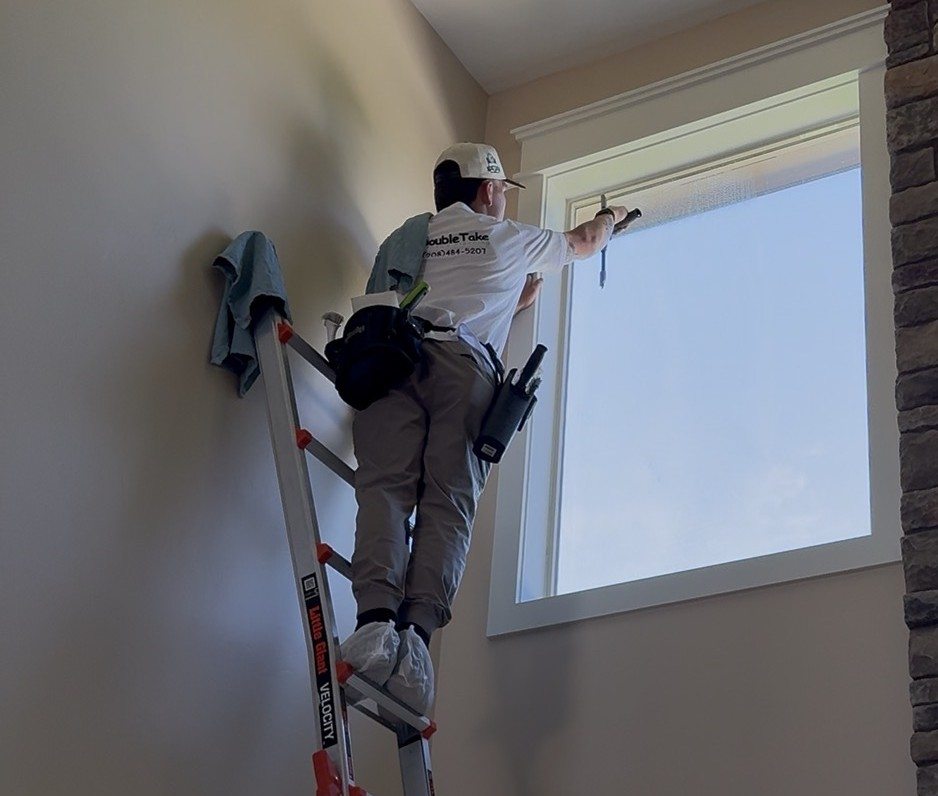Double Take tech on a ladder squeegeeing a high indoor window.