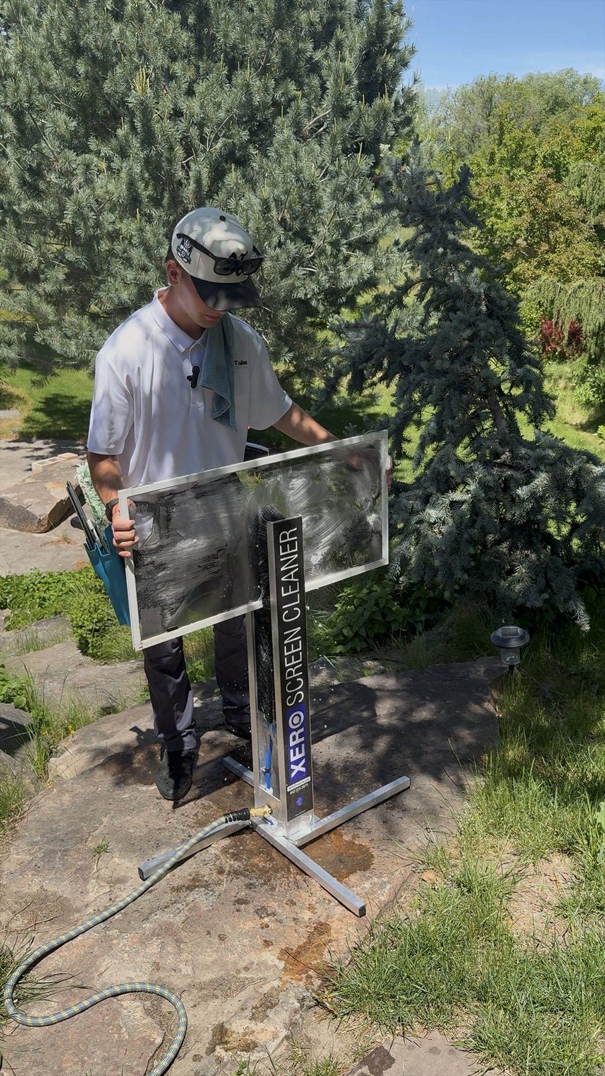 Double Take tech running a window screen through a XERO screen cleaning machine on a stone patio.