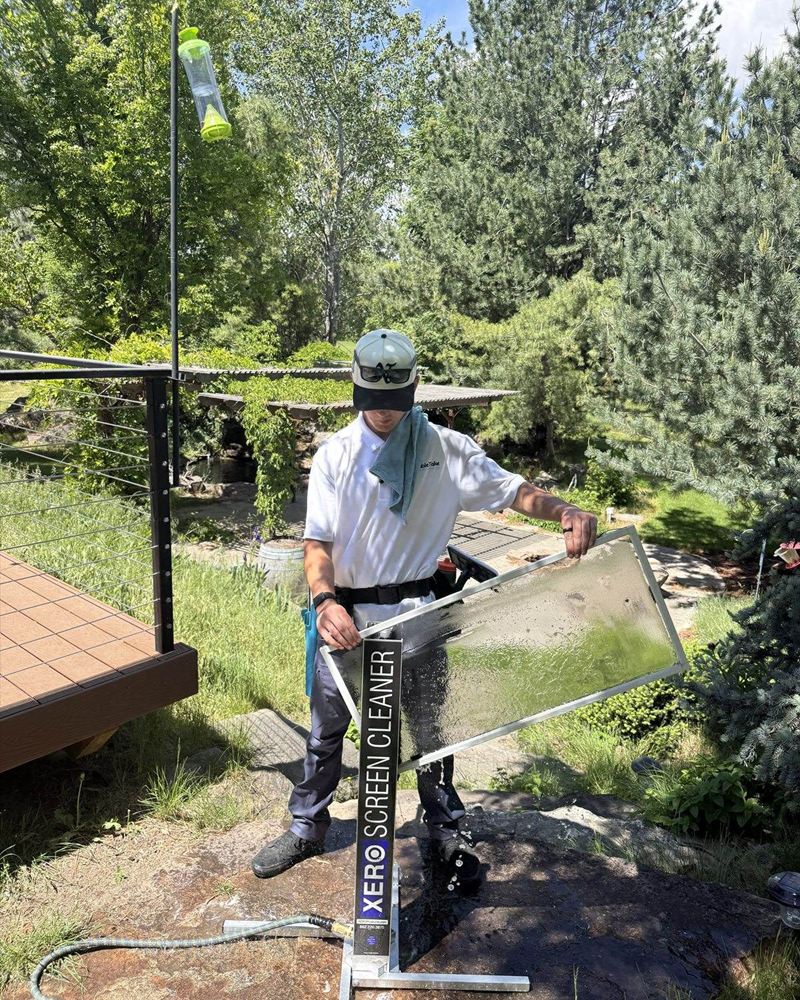 Professional cleaner uses a Xero Screen Cleaner machine to wash a window screen outdoors.